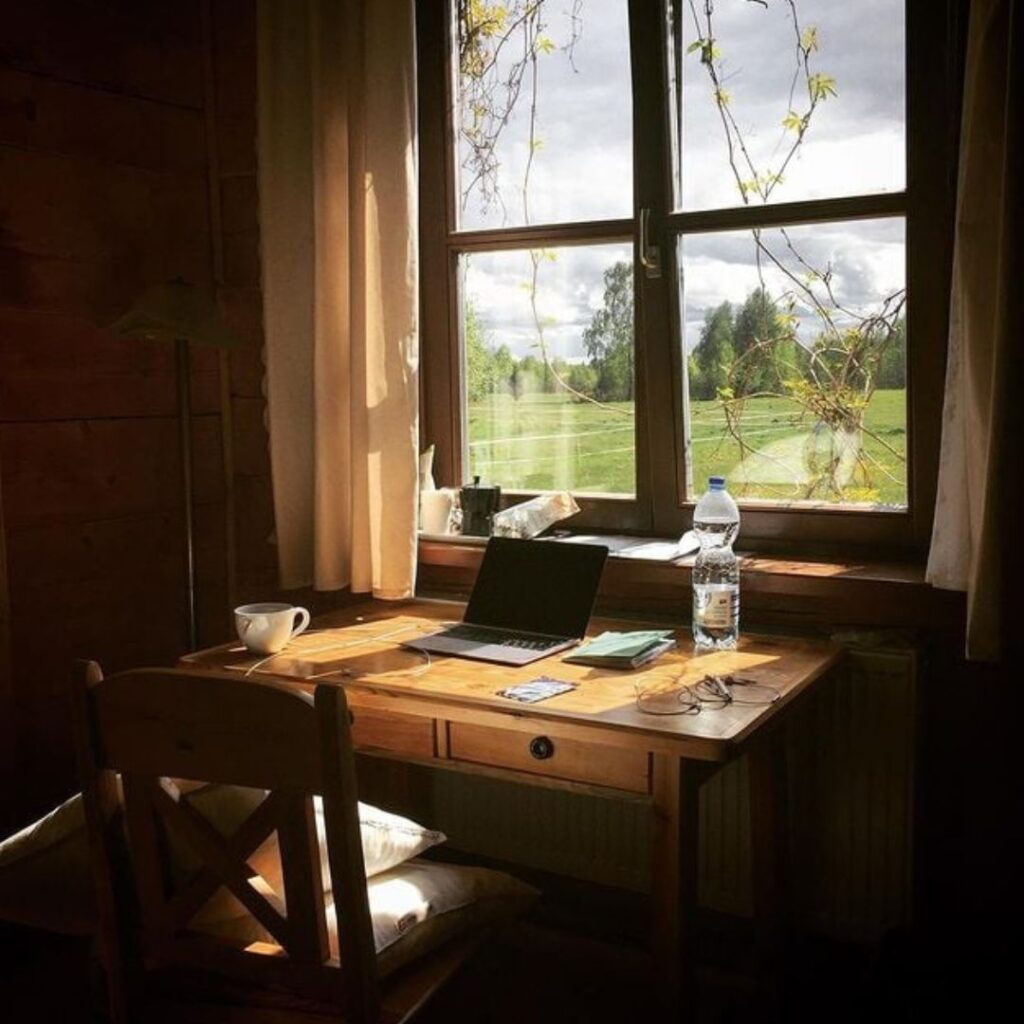 biurko z laptopem przy oknie z widokiem na łąki